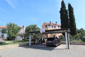 A covered parking area with a basketball hoop, a car, and a scooter.