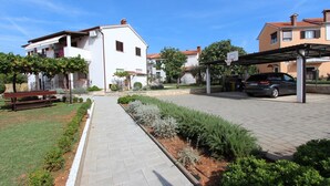 Zona residencial con un sendero pavimentado, una cancha de baloncesto y un coche estacionado.