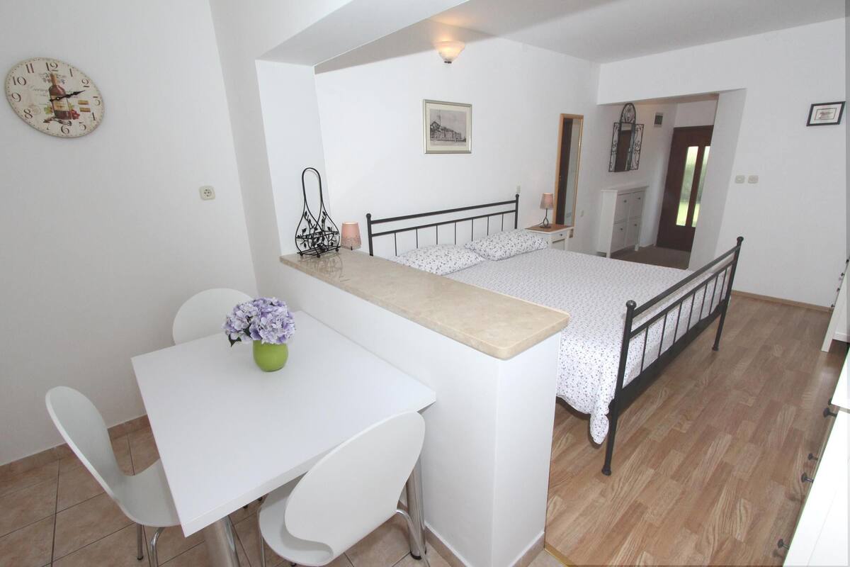 A compact bedroom with a bed, bedside table, and a small desk area with a chair and a vase of flowers.