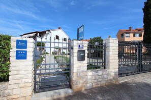 A gated entrance to a building with a stone wall and metal gate, a sign indicating 'APARTMAN' and 'STUDIO APARTMAN', and a blue sign with '10 BETTERENER'.
