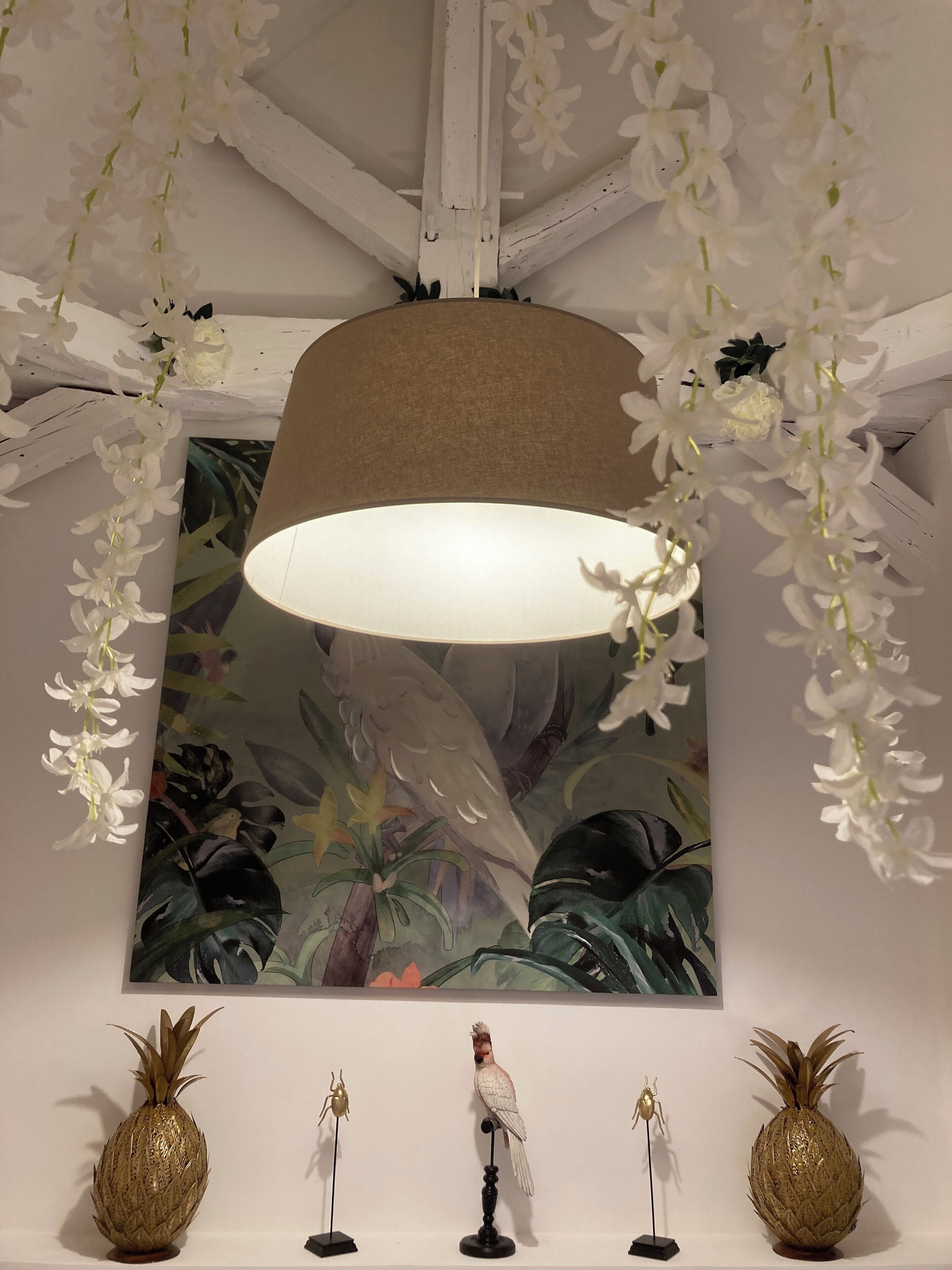 Een kamer met een groot raam, een hanglamp en twee gouden ananassculpturen op de vloer.