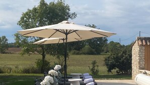 An outdoor seating area with lounge chairs, tables, and a large umbrella. - charming cottage at the gates of Issigeac (Montaut D'issigeac)