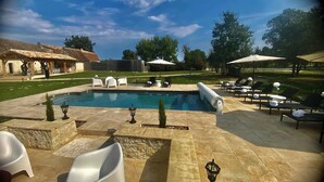 A swimming pool with lounge chairs and umbrellas, surrounded by a stone patio and a wooden pergola. - charming cottage at the gates of Issigeac (Montaut D'issigeac)