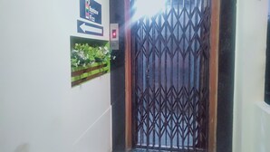 A door with a metal security gate, a wall-mounted sign indicating a direction, and a small planter with flowers. - Choice Service Apartment (Pune)