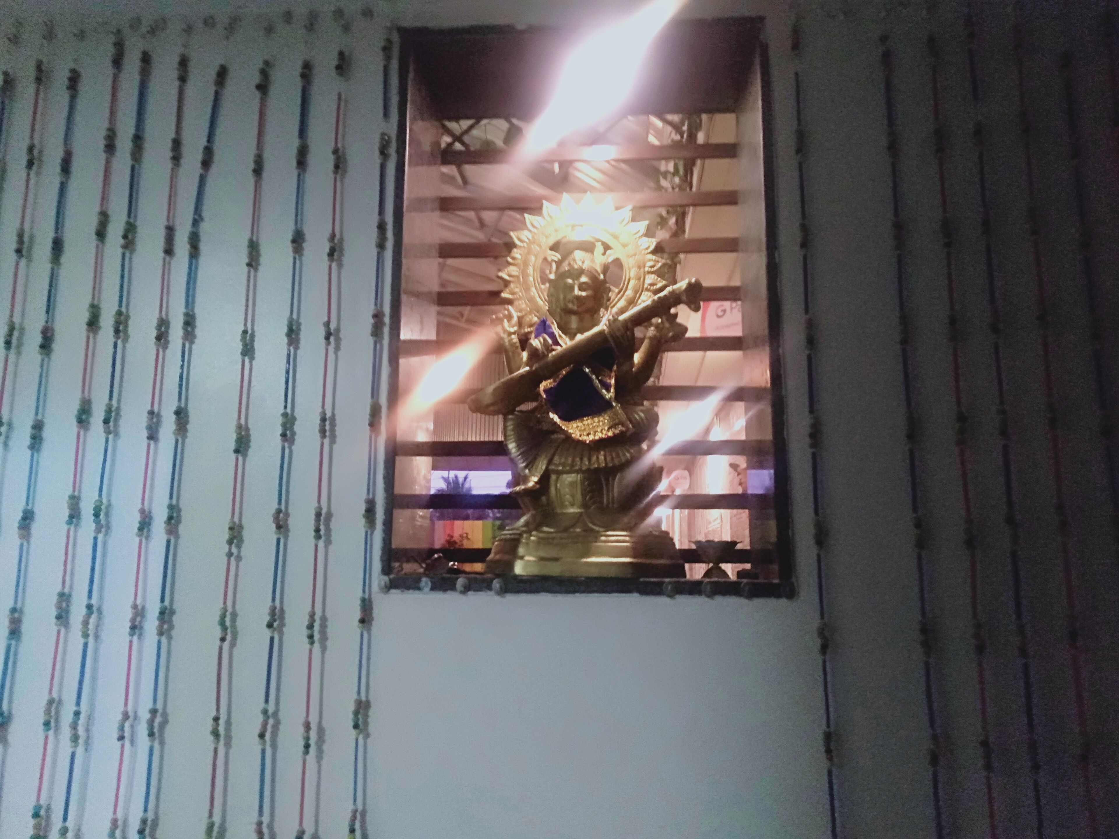 A statue in a window with vertical blinds.