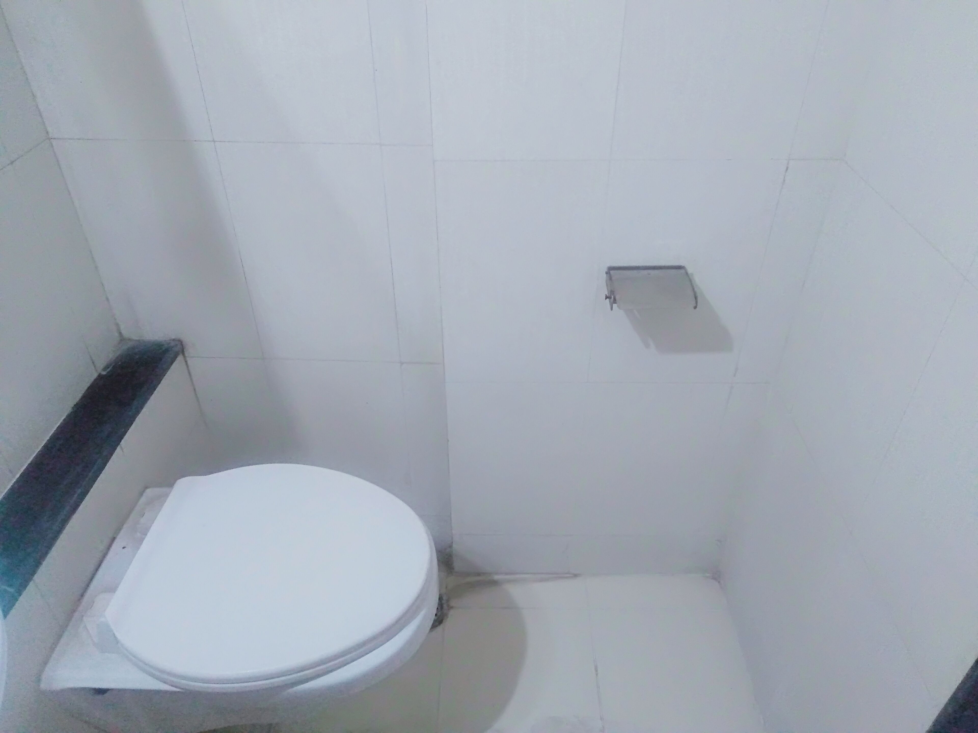 Un baño pequeño y estrecho con un inodoro blanco y un perchero metálico en la pared.