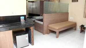 A compact kitchenette with a refrigerator, a small sink, and a countertop. There is a bench with a cushion for seating, and a small table with a telephone. - Choice Service Apartment (Pune)