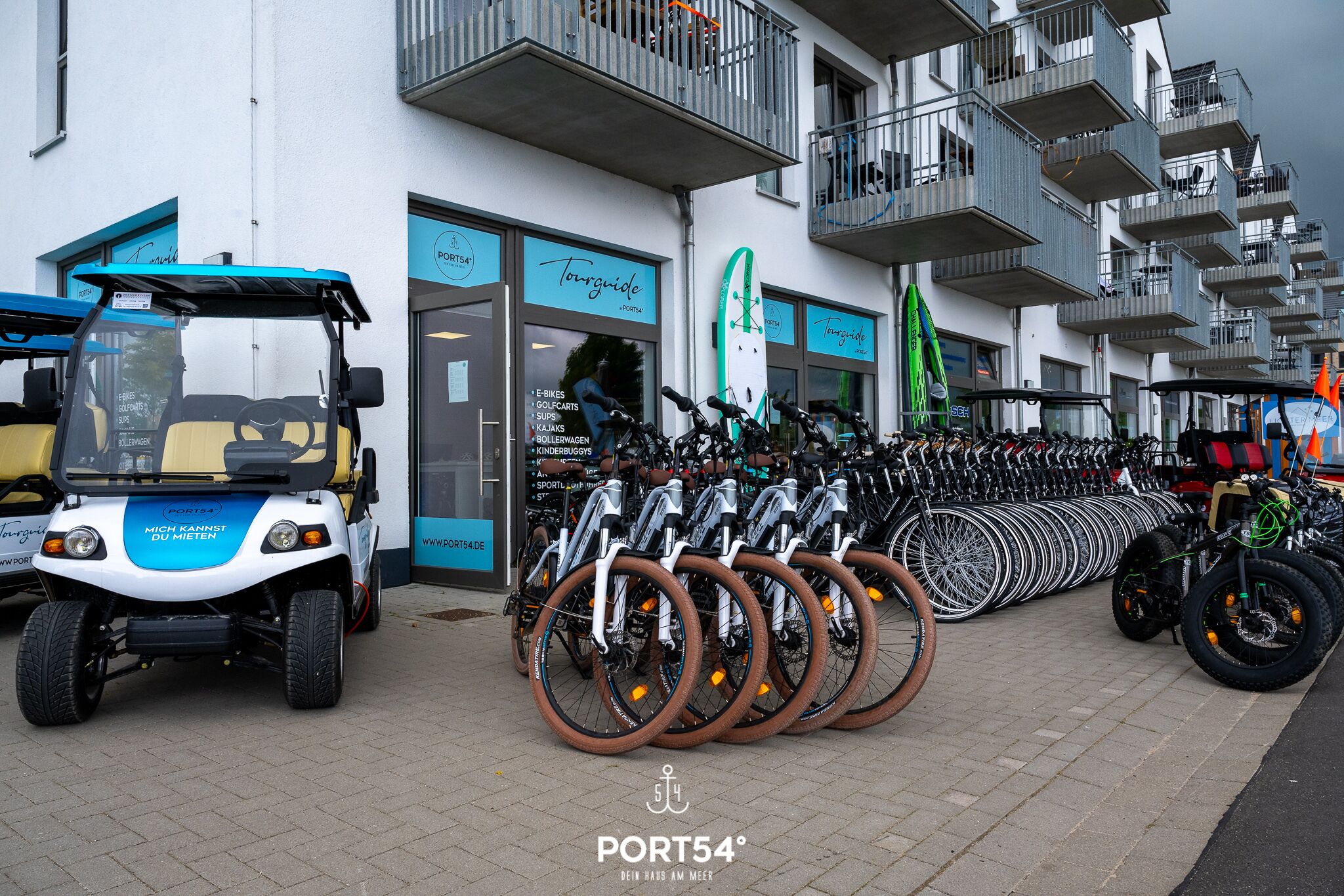 En rad cyklar står uppradade utanför en byggnad med en skylt där det står ”Port54”.