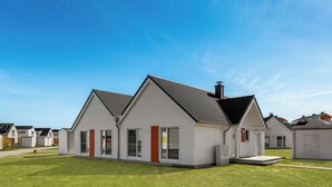Une maison moderne à deux étages, dotée d’un toit en pente, de grandes fenêtres et d’une pelouse bien entretenue.
