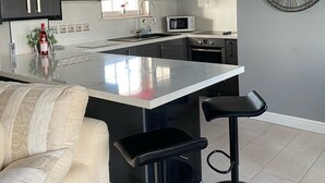 A modern kitchen with a central island, bar stools, a clock on the wall, and pendant lighting. - Cumberland stable lodge  (Workington)