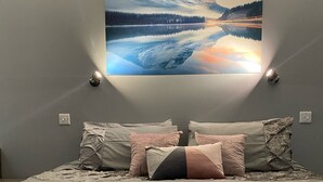 A bedroom with a bed, pillows, and a wall-mounted painting of a mountain landscape. - Cumberland stable lodge  (Workington)