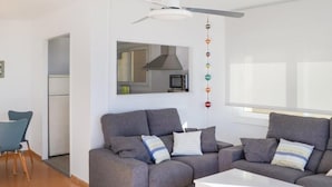 A modern living room with a grey sofa set, a white coffee table, and a kitchen area visible in the background.