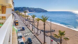 A coastal road with parked cars, palm trees, and a beach in the background.