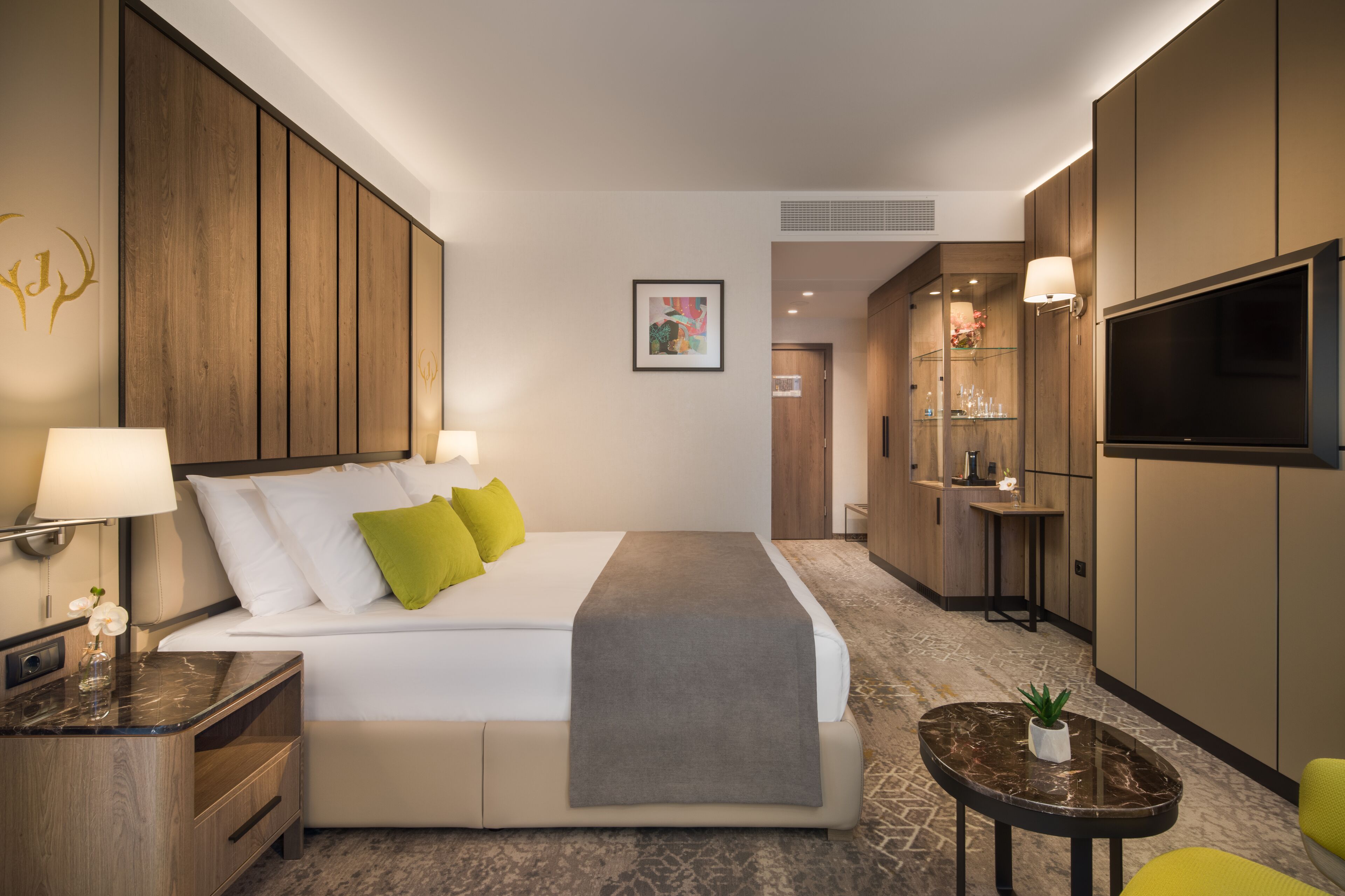 Een hotelkamer met een bed, nachtkastjes, een televisie, een klein tafeltje met een plant, en een badkamer op de achtergrond.