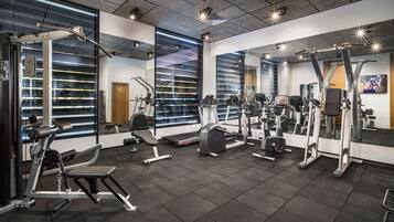 A modern gym with various exercise equipment, large windows with blinds, and a mirror wall.