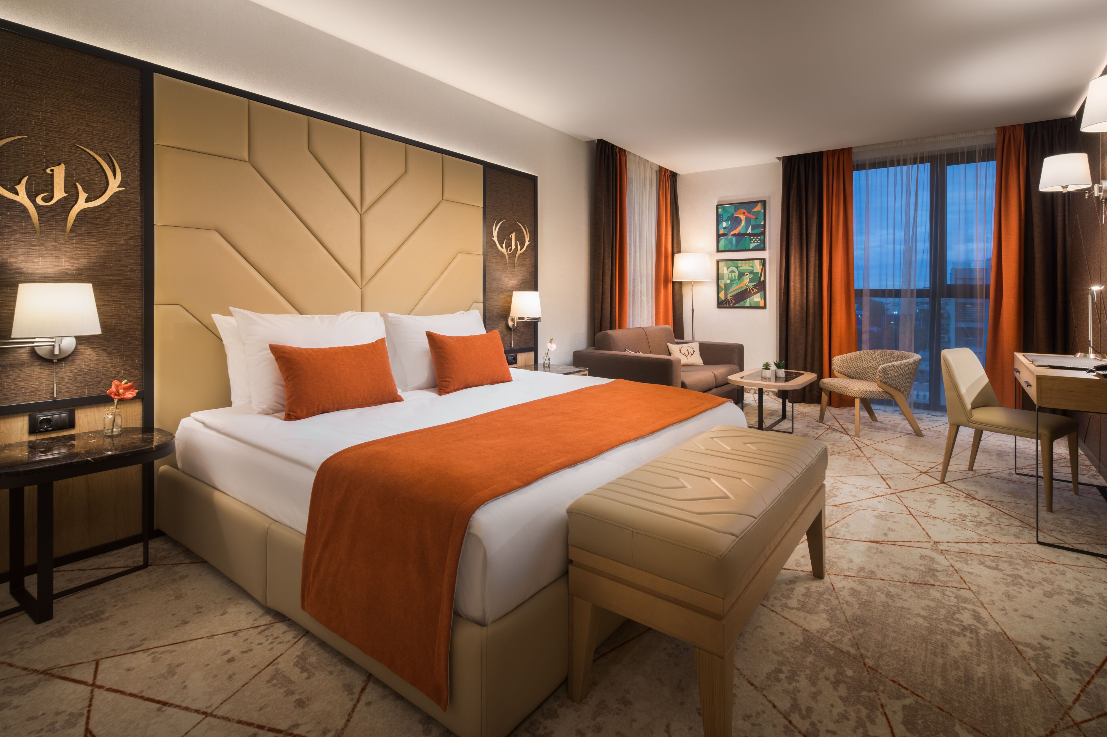 A hotel room with a large bed, a desk, a chair, a sofa, and a small table.