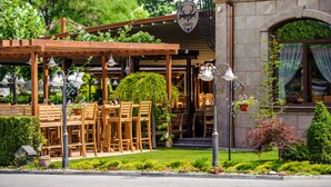 An outdoor seating area with wooden tables and chairs, surrounded by greenery and a building with a stone facade. - Hotel Jägerhof (Plovdiv)