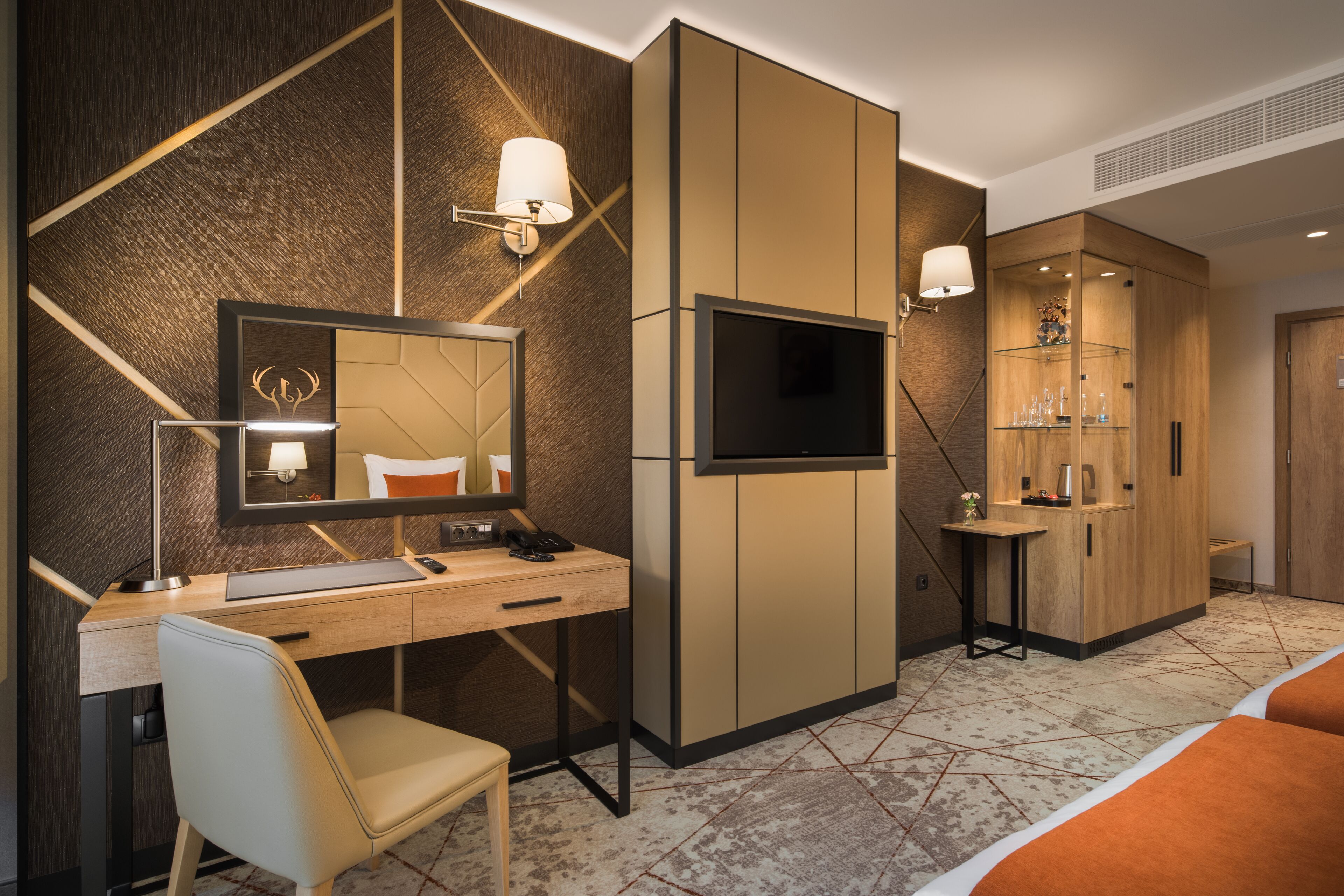 A modern hotel room with a desk, chair, TV, and a minibar.