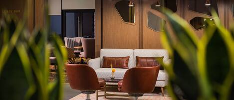 A lobby with a white sofa, two brown armchairs, and a coffee table. There are hanging pendant lights and a plant in the foreground.