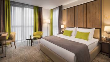 Una habitación de hotel con una cama grande, dos lámparas de noche, un escritorio con una silla y una mesita con una planta.