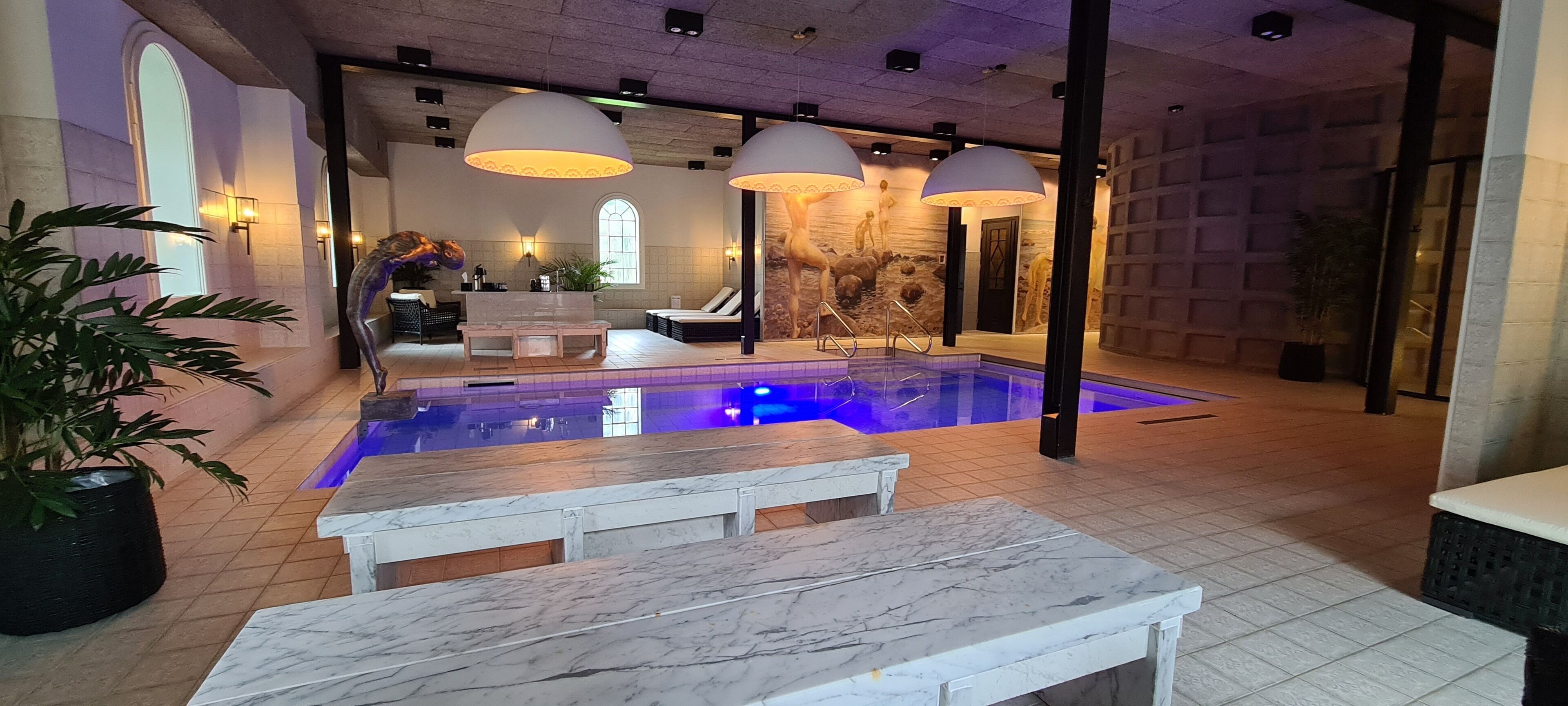 A pool area with a marble bench, lounge chairs, and a stone wall with sculptures.
