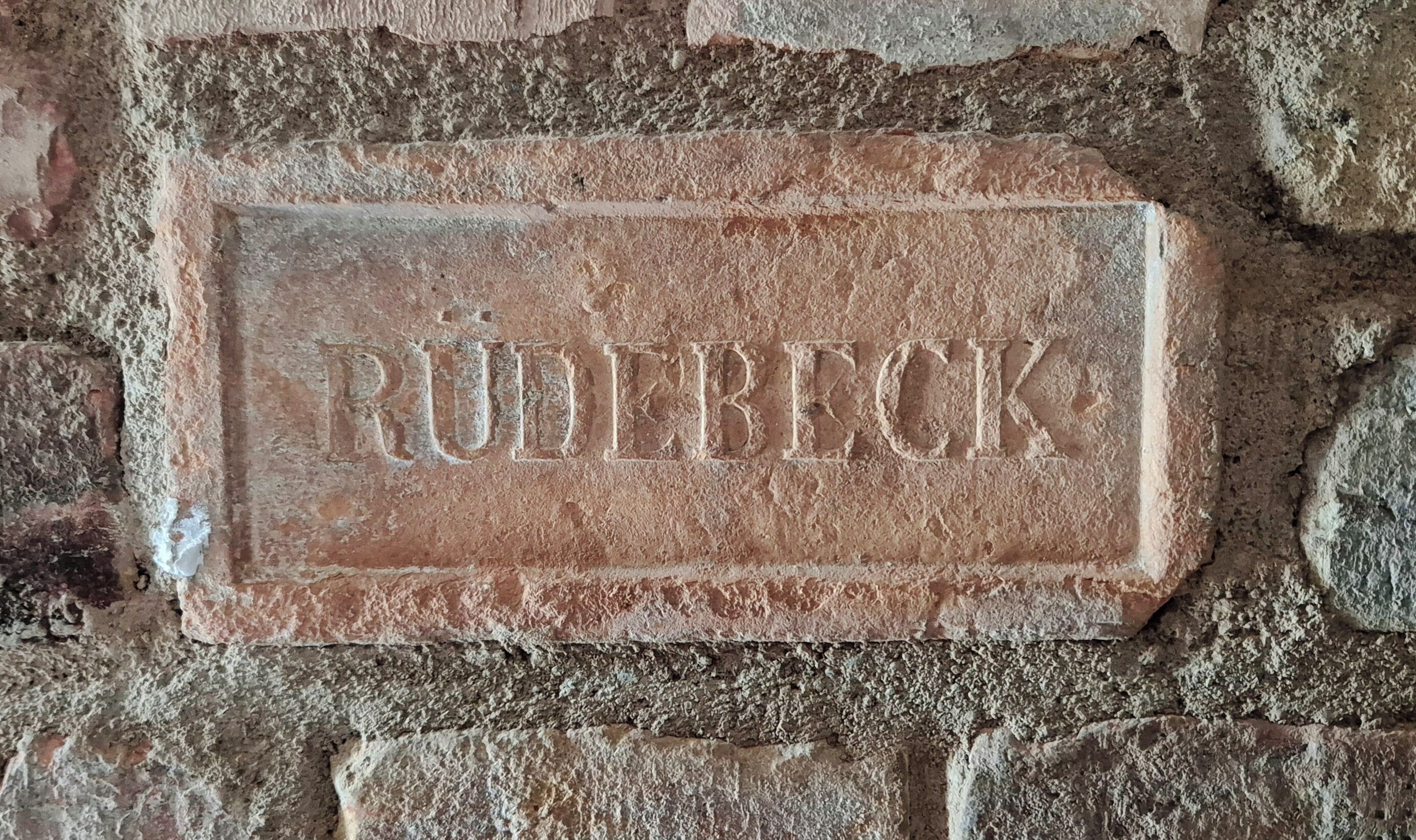 A stone plaque with the inscription "RÜDERECK" on a brick wall.