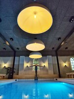 Una piscina con múltiples luces en el techo, una estatua en el centro y muros de piedra con ventanas.
