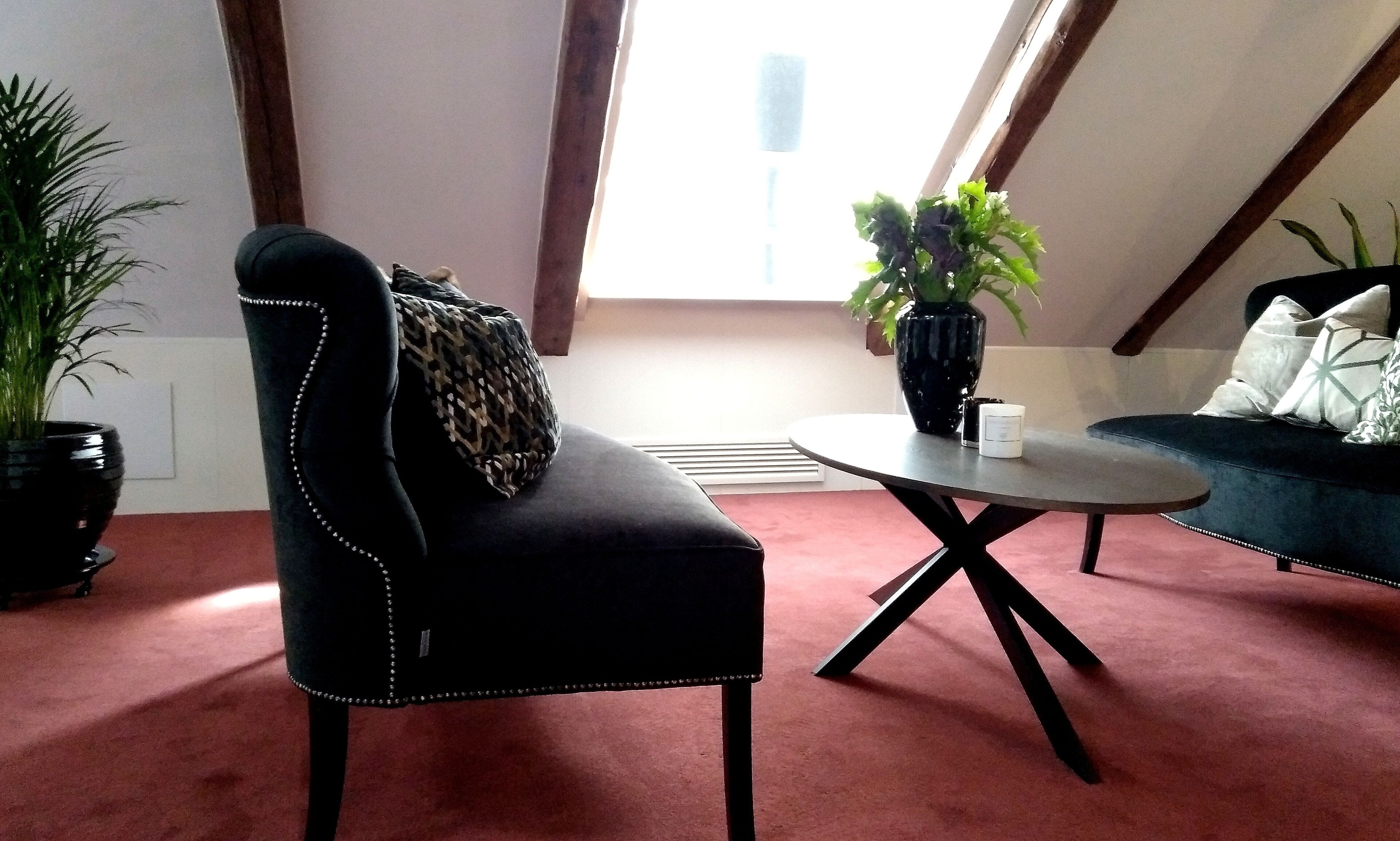 A room with a black upholstered chair, a round coffee table, a sofa, and a potted plant.