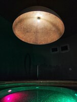 Una lámpara de techo grande, redonda y con textura en una habitación con poca luz, suelo de baldosas y un poste visible.
