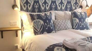 Een opgemaakt bed met beddengoed met een patroon, een nachtkastje met een lamp en een wandplank.