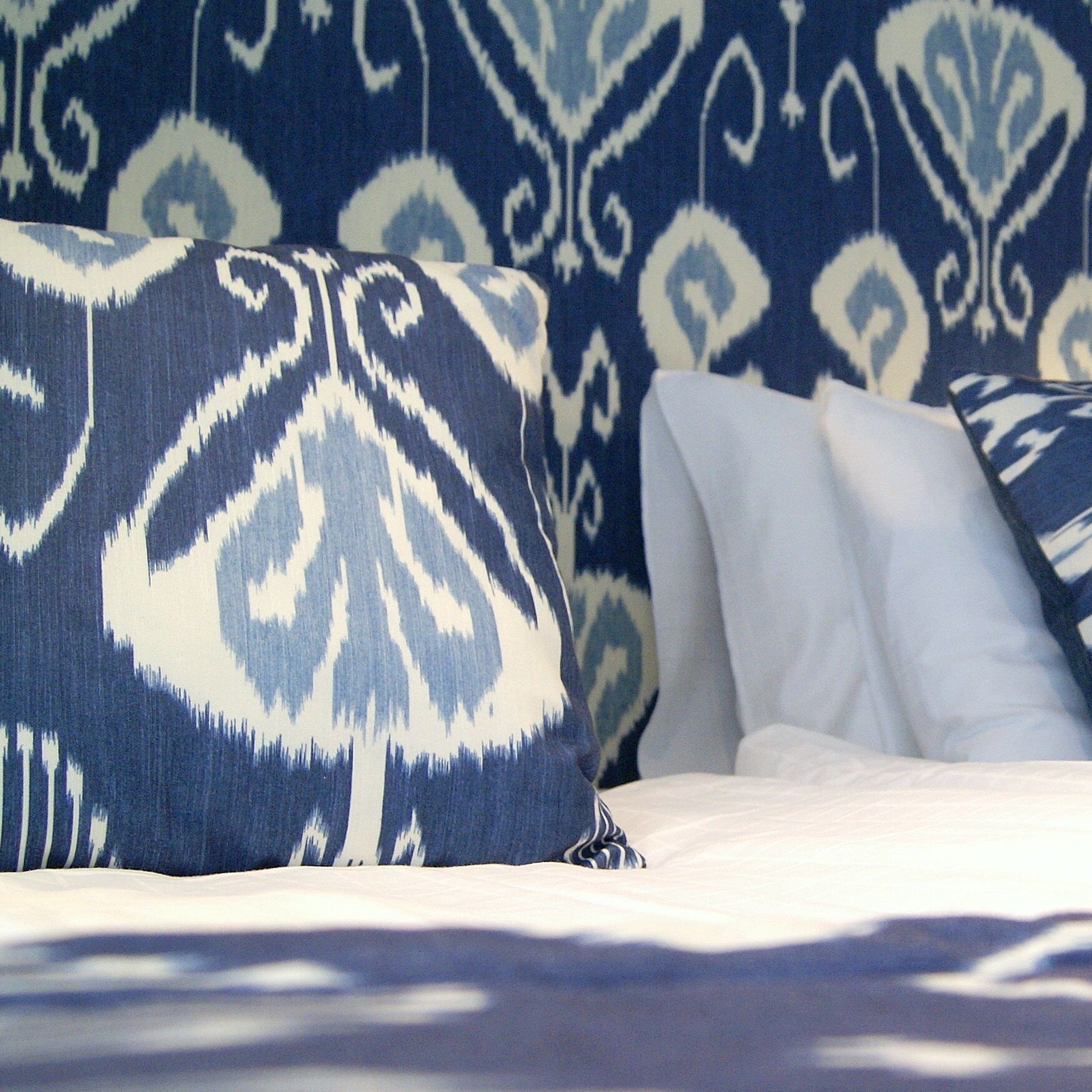 A bed with patterned pillows and a patterned wall.