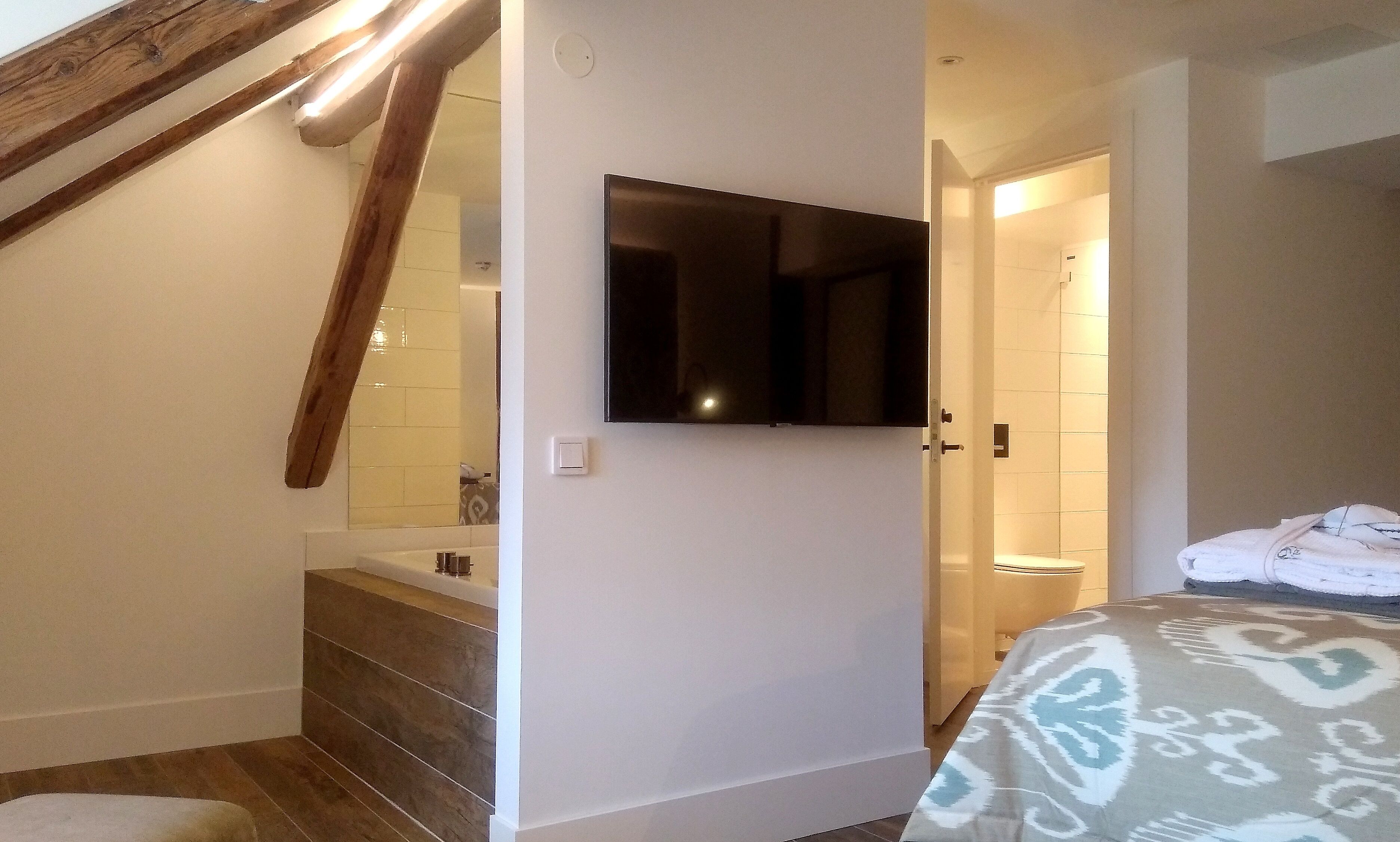 Un dormitorio con cama, un baño con bañera y un televisor montado en la pared.