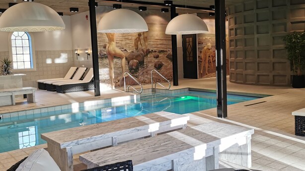 Un área de piscina interior moderna con una piscina cristalina, sillas de descanso y un mostrador de recepción.