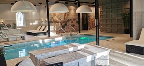 Un área de piscina interior moderna con una piscina cristalina, sillas de descanso y un mostrador de recepción.