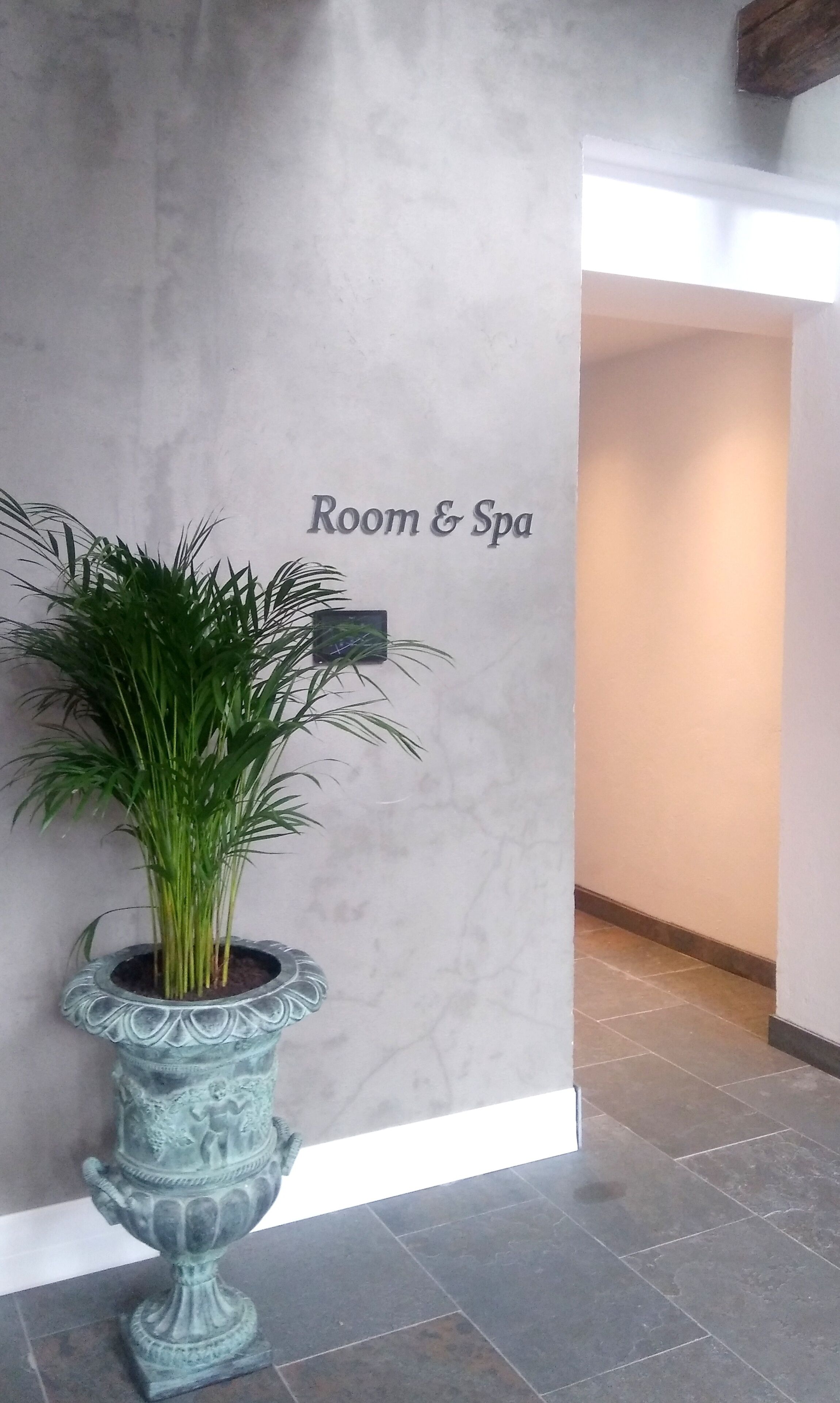 A reception area with a 'Room & Spa' sign on the wall, a potted plant, and a tiled floor.