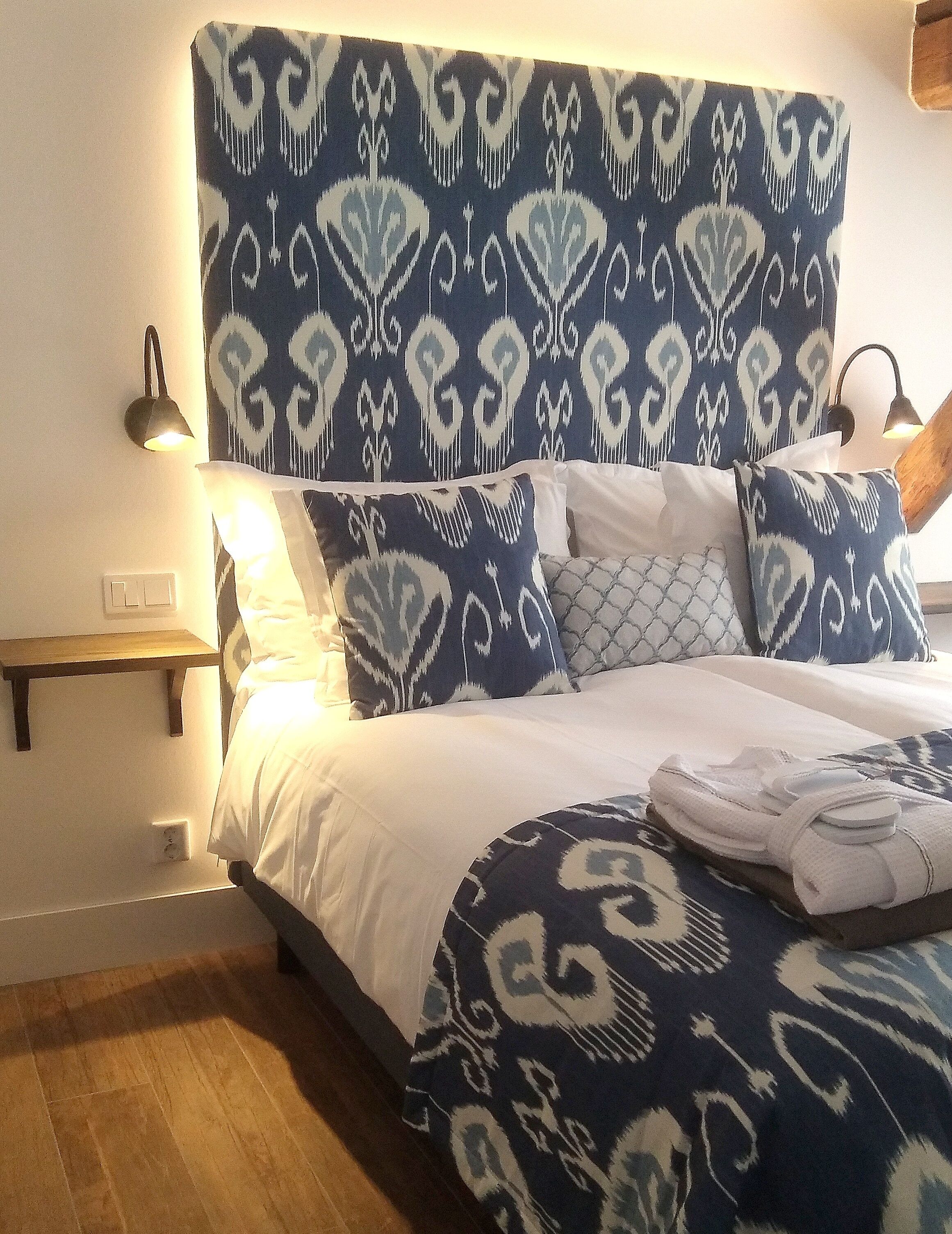 A bed with a patterned headboard, a bedside lamp, and a wooden nightstand with a lamp.