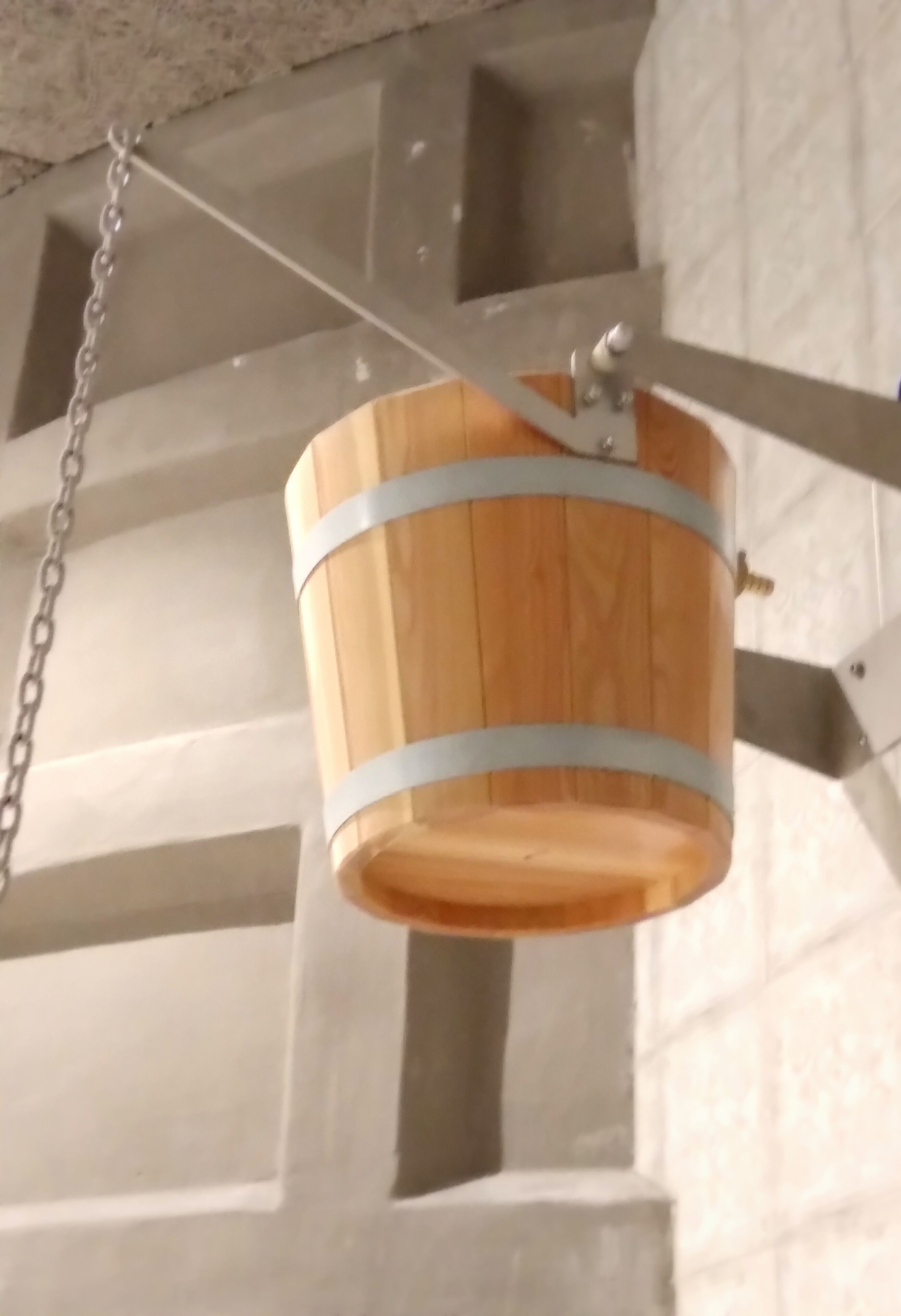 A wooden bucket hanging from a metal fixture with a chain.