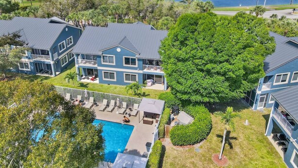 A large blue house with a swimming pool, surrounded by lush greenery and a lake.