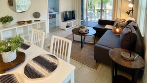 A modern living room with a dining area, a sofa set, a TV, and a balcony with a view.