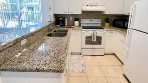 A modern kitchen with white cabinets, granite countertops, a built-in oven, and a microwave.