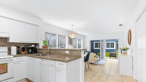 Uma cozinha moderna com armários brancos, bancada de granito e área de jantar com sofá azul e máquina de café.