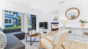 Uma sala de estar moderna com sofá, poltrona, televisão e um espaço de jantar com mesa e cadeiras.