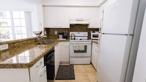 A compact kitchen with white cabinets, a granite countertop, a stove, an oven, a microwave, and a refrigerator. - 320B - Boca Retreat w/ Pool, Parking, Near Evert Tennis & Shops (Boca Raton)