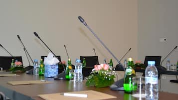 A conference room with a long table, microphones, water bottles, and a flower arrangement.