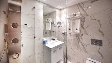 A modern bathroom with a glass-enclosed shower, a white sink, and a marble backsplash.