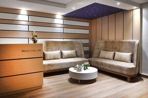 Un área de recepción con un mostrador identificado como "RECEPTION SPA", dos sofás, una mesa de centro redonda con adornos y un techo con diseño de estrellas.