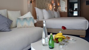 A hotel room with a bed, a sofa, a table with a bottle, glasses, and fruit. - Flower Town Hôtel & Spa (Rabat)