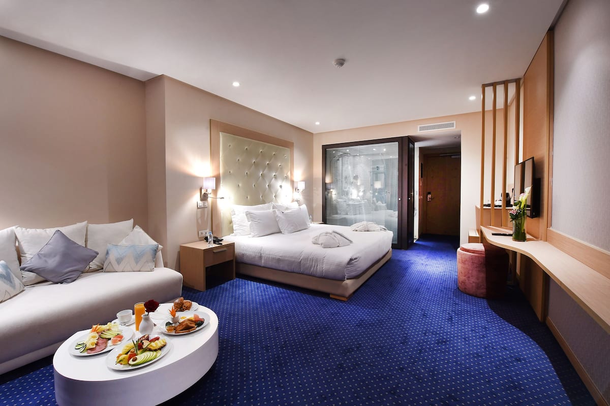 A hotel room with a bed, a sofa, a dining table with breakfast, and a TV.