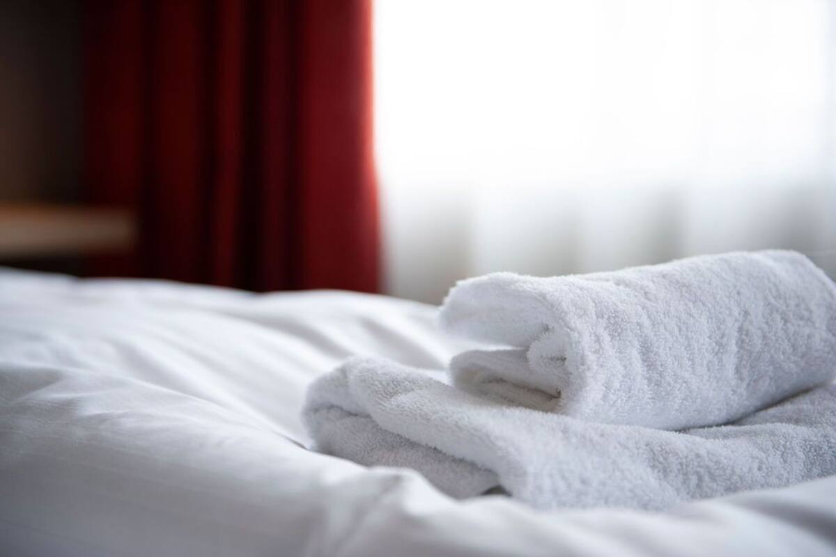 A neatly made bed with white linens and a folded white towel on top.