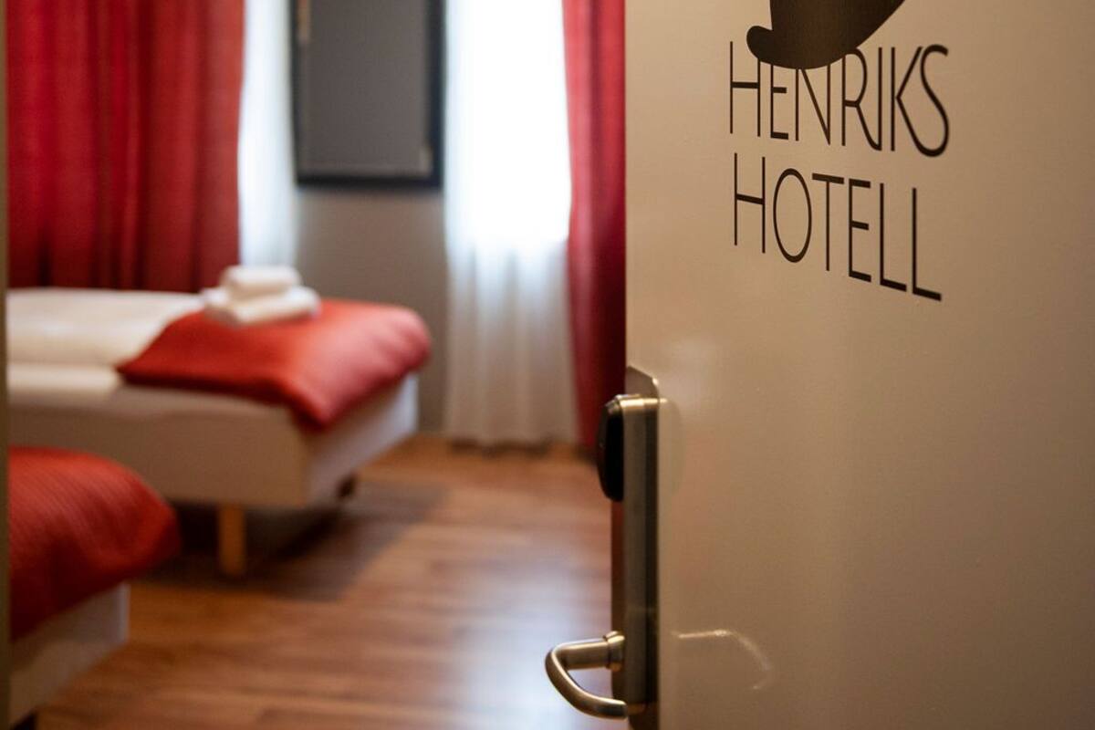 A hotel room with a bed, a red curtain, and a wall with the text "Henriks Hotel".
